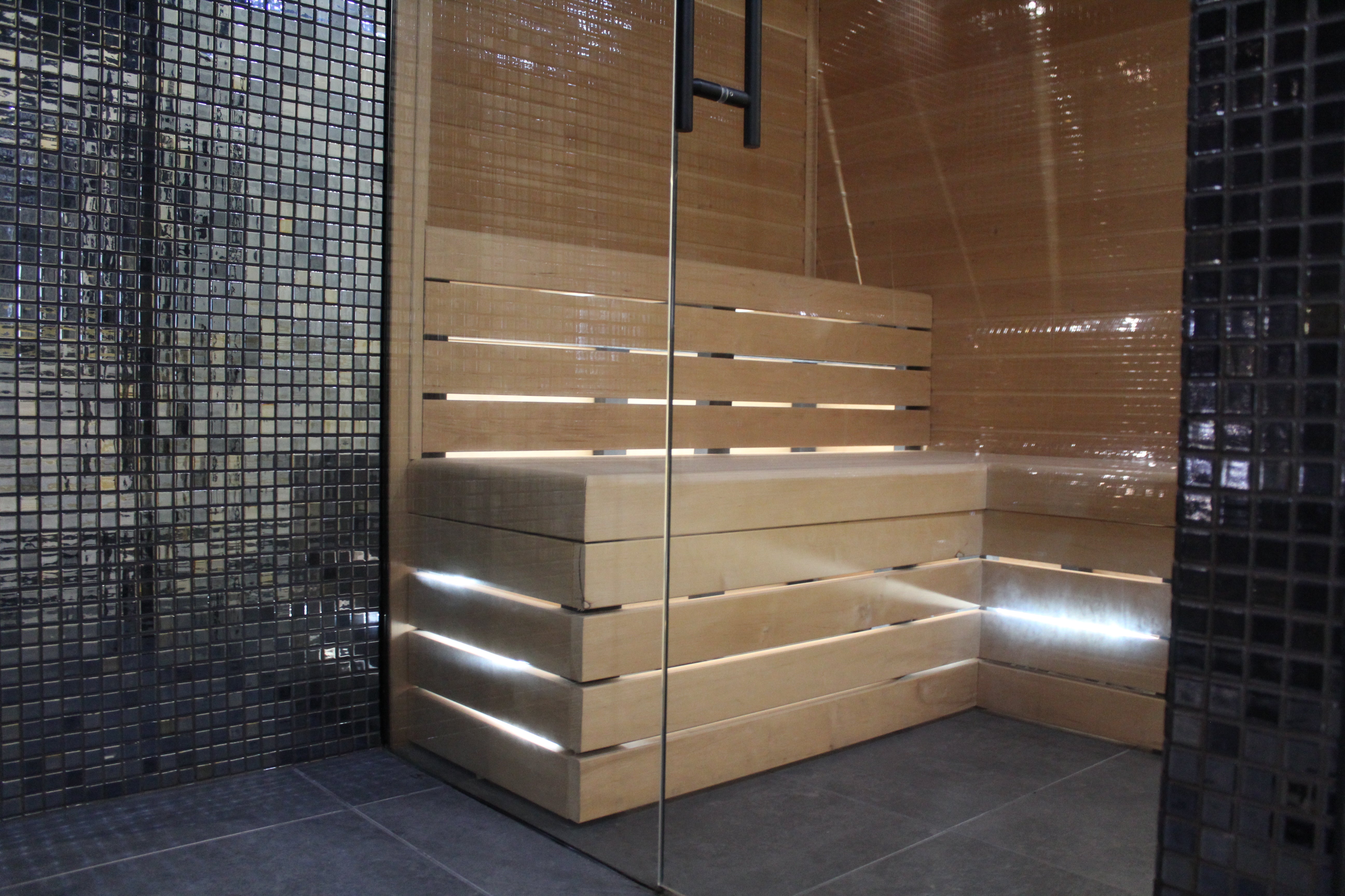 Wooden bench in a steam room with black mosaic tiles on the walls.
