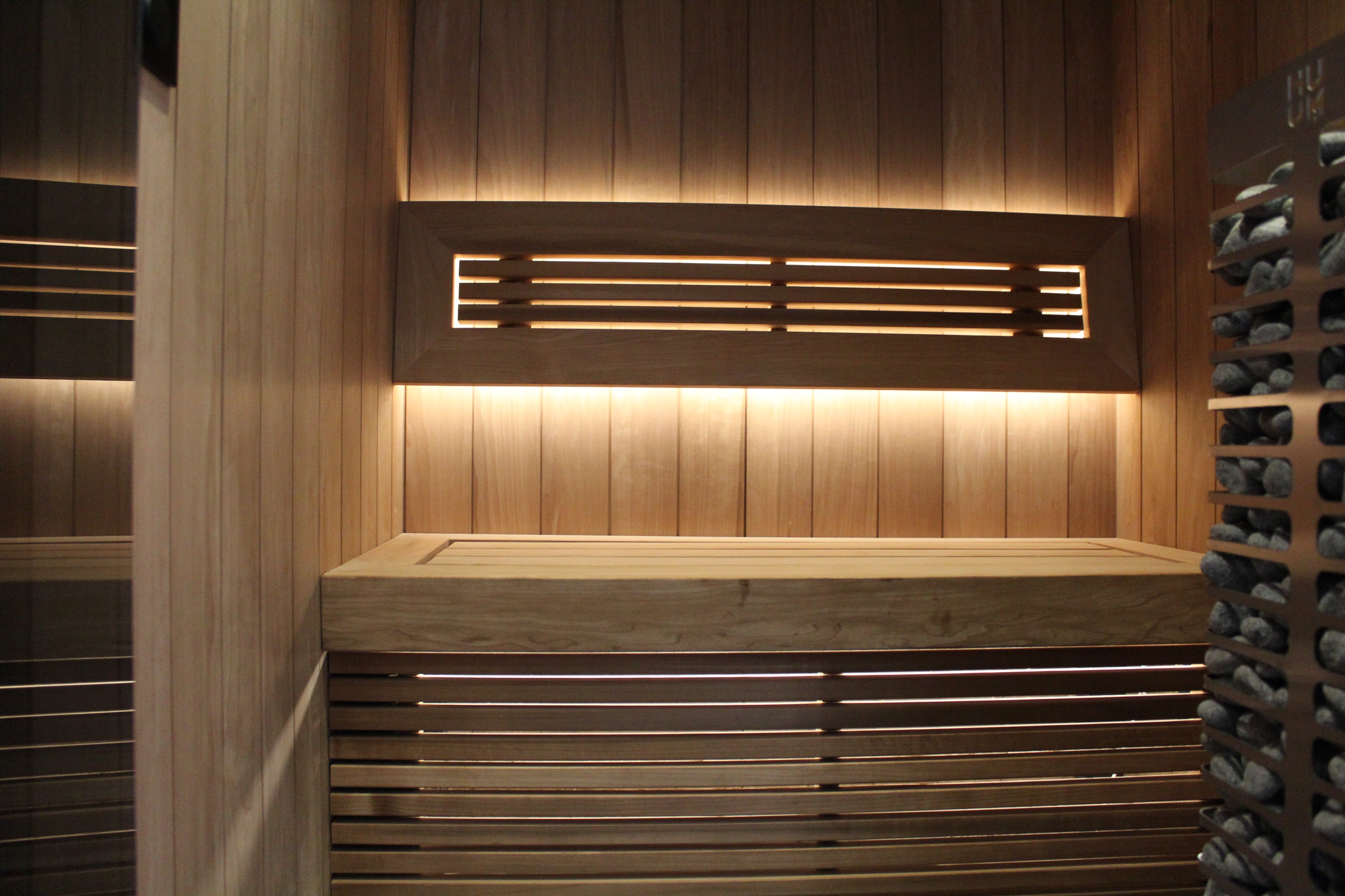 Wooden sauna with a bench and wall panels, illuminated by warm back lights.