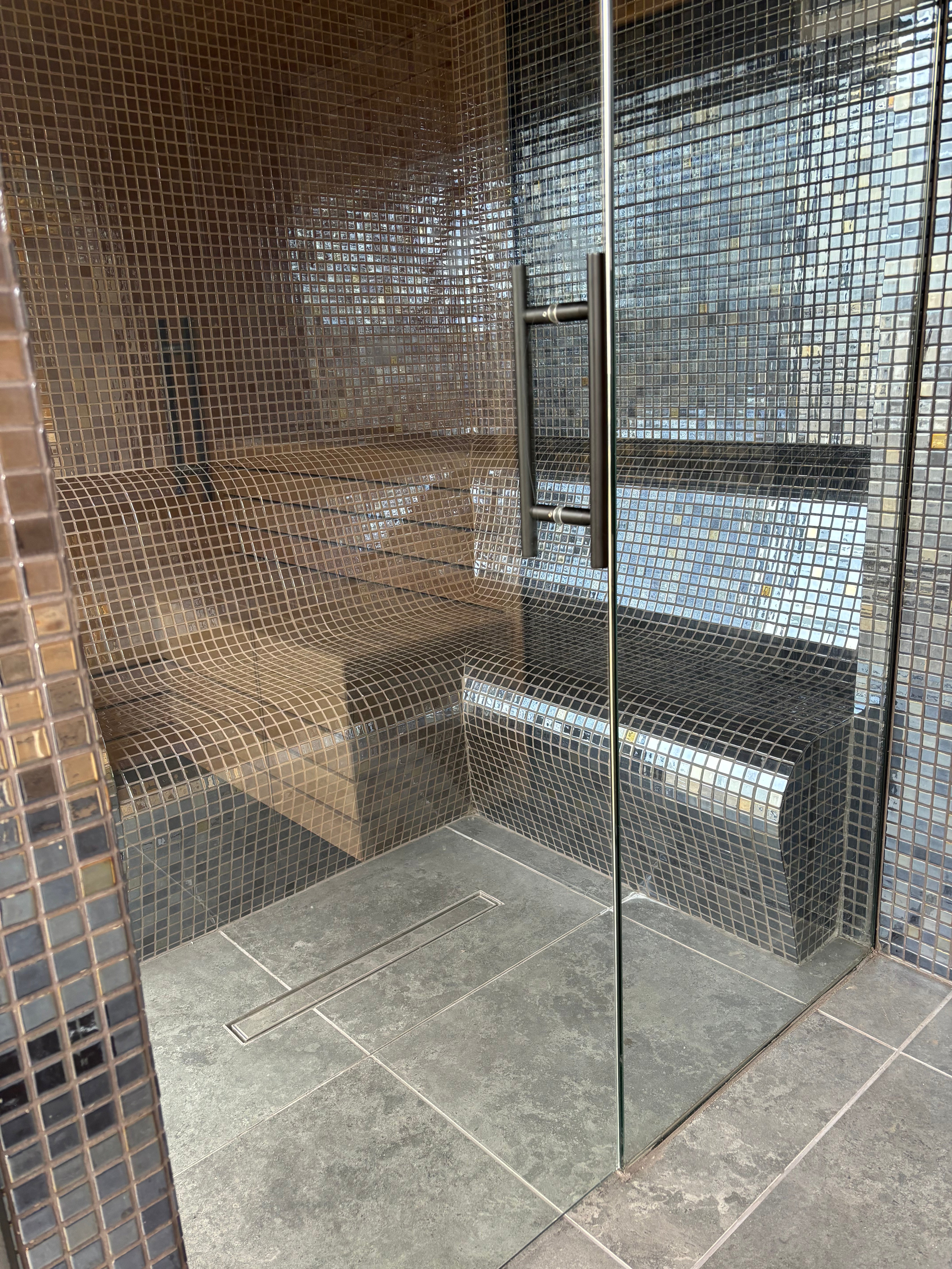 Glass-enclosed steam room with mosaic tile walls and floor.