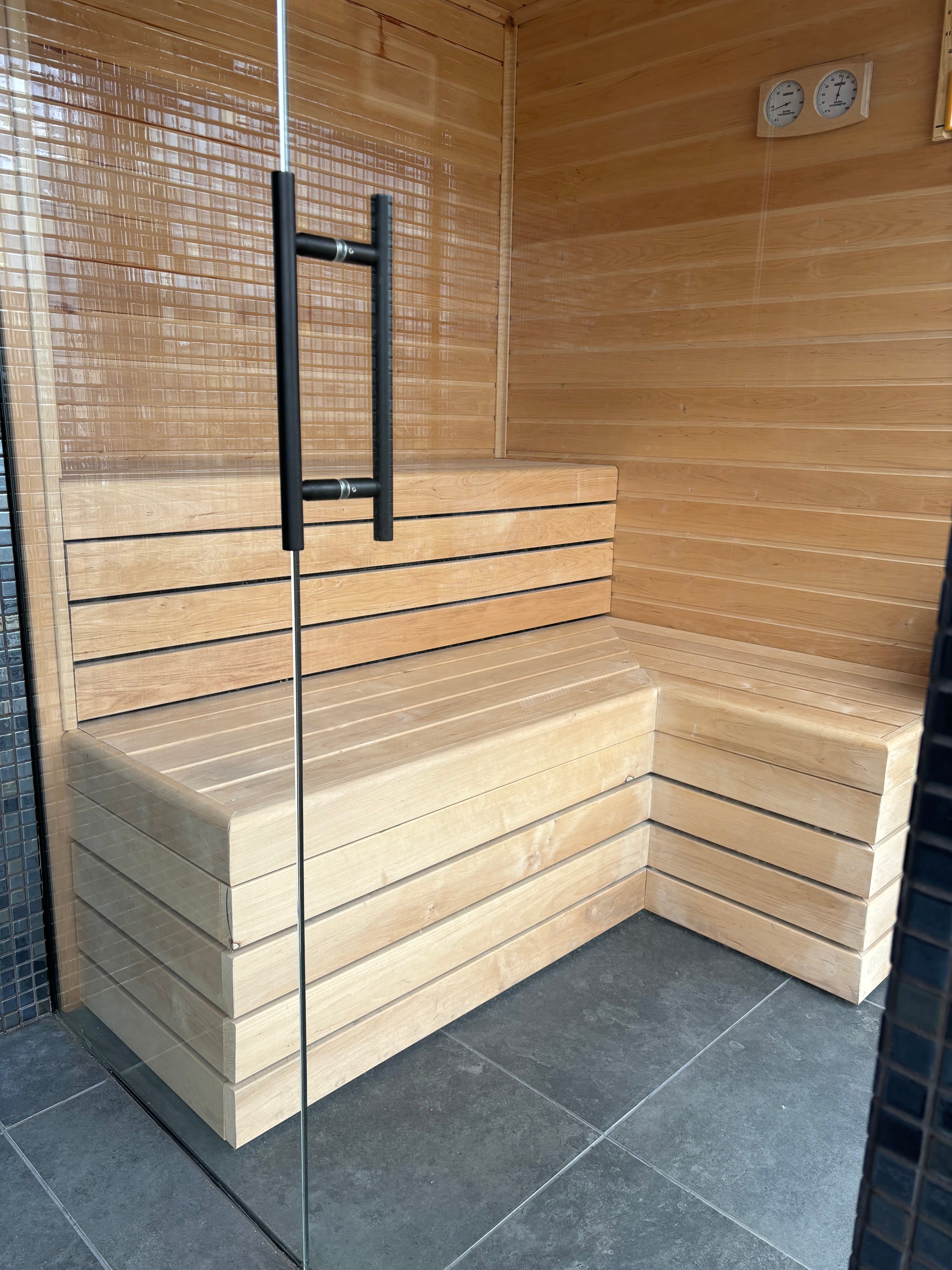 Wooden sauna with bench and glass door next to a tiled room