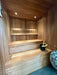 Wooden sauna with benches, a bucket, and a stone sauna heater on a tiled floor.