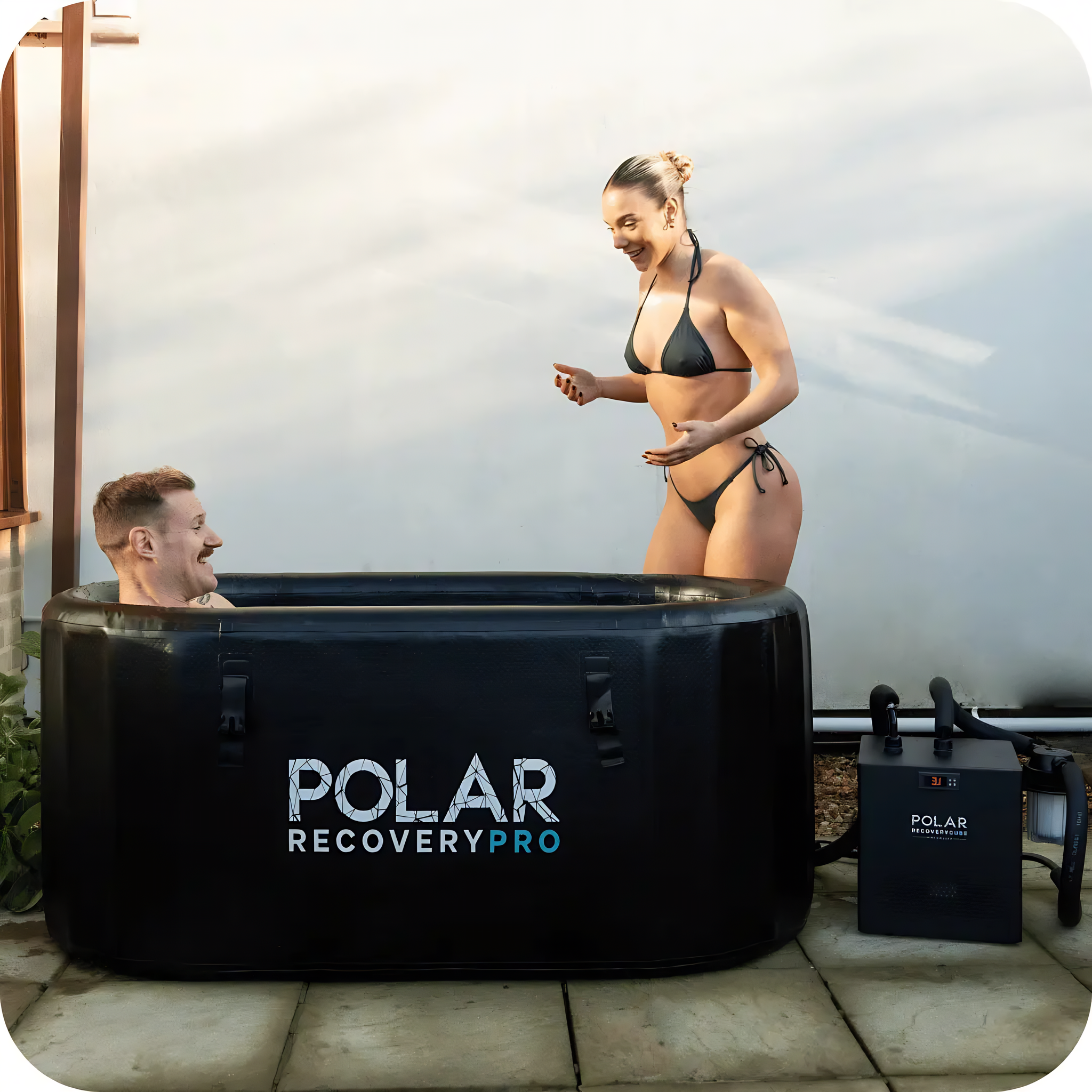 Polar Recovery Pro inflatable ice bath in black, couple laughing beside the chiller, alternate view
